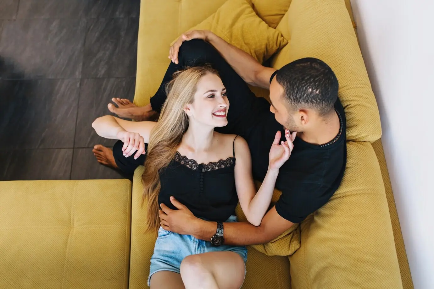 Ein verliebtes Paar umarmt sich, liegt auf dem Sofa und schaut sich an. Eine junge Frau berührt das Gesicht des Mannes. Warme Beziehung, Romantik, Hauskleidung, Erholung.